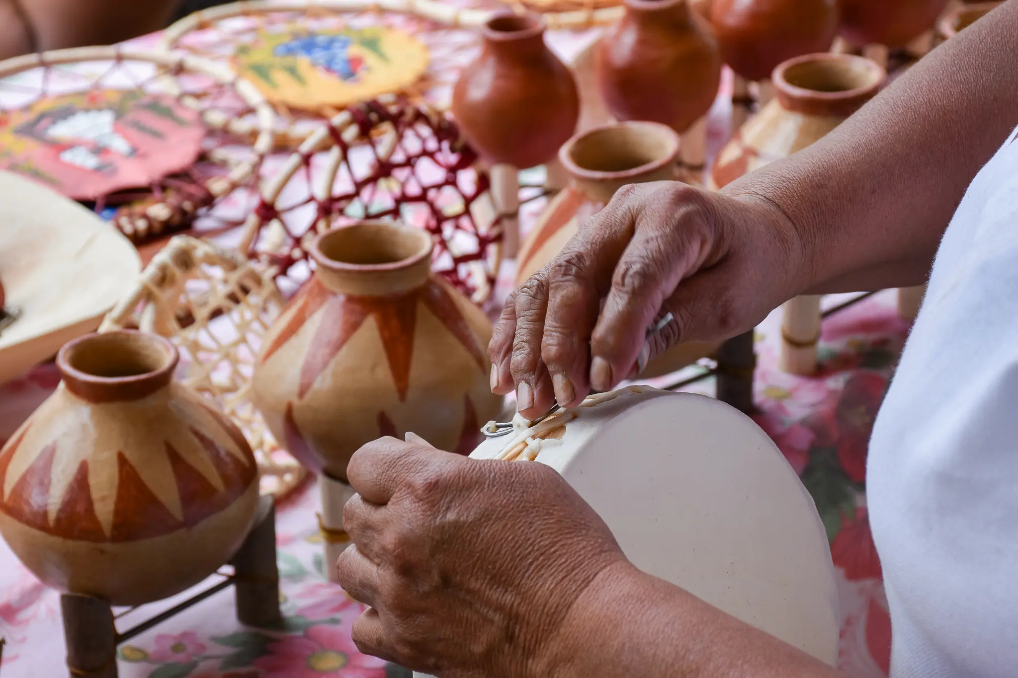 Manos artesanas ajustando un tambor junto a vasijas de cerámica en una mesa de trabajo.